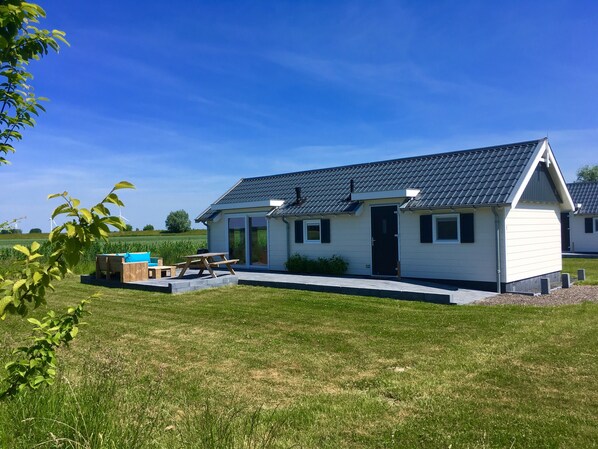 A small, single-story house with a dark roof, a front door, and a patio with a table and chairs. - Chalet for 4 persons in Kamperland, close to beach and sea (kamperland)