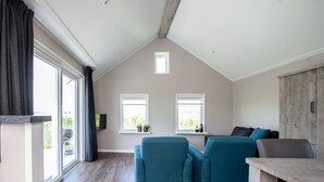 A modern living room with a sloped ceiling, two windows, a sofa set, and a wooden table. - Chalet for 4 persons in Kamperland, close to beach and sea (kamperland)