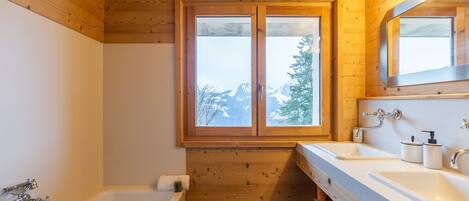 Un baño con paneles de madera, un ventanal grande, dos lavamanos y una bañera.