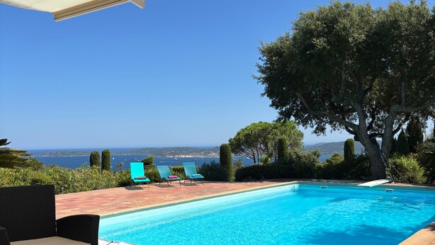 Una piscina con agua cristalina azul, rodeada de sillas de descanso y vistas al mar.