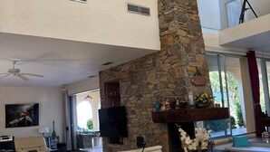 Amplia sala de estar con chimenea de piedra, asientos cómodos, televisor de pantalla plana y un ventanal con vistas al exterior.