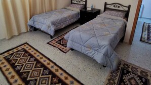A bedroom with two single beds, a nightstand, a window with curtains, and patterned rugs. - Olive Palace Restaurant and Lounge  (al-Khader)