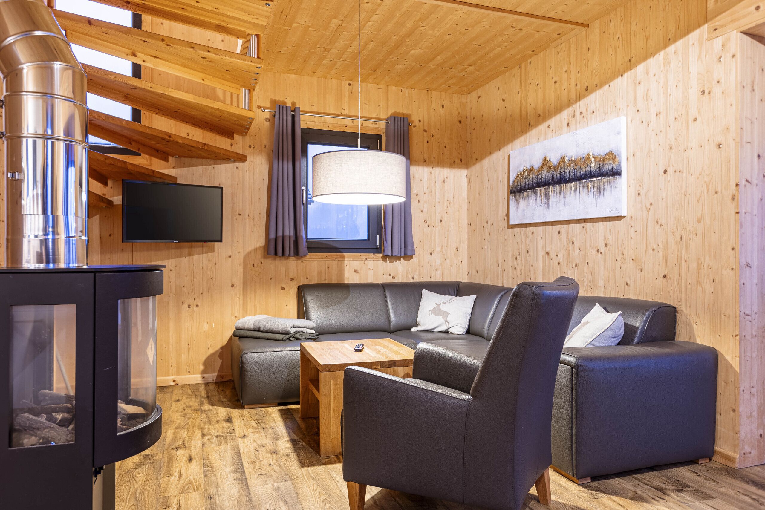 L’intérieur d’un chalet chaleureux, avec une cheminée, un canapé en cuir et un tableau accroché au mur.