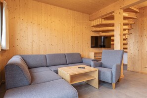 Ein Holzinnenraum mit einem Ecksofa, einem einzelnen Sessel, einem Couchtisch und einem an der Wand befestigten Flachbildfernseher.