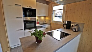 Una cucina moderna con mobili bianchi, elettrodomestici in acciaio inossidabile, forno integrato, lavello e finestra con vista esterna.