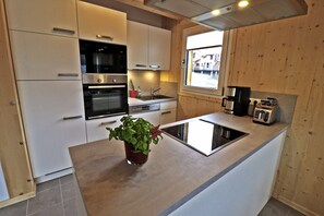 A modern kitchen with white cabinetry, stainless steel appliances, a built-in oven, a sink, and a window providing a view outside.