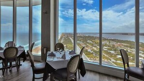 A dining area with a table set for four, large windows offering a view of a coastal cityscape.