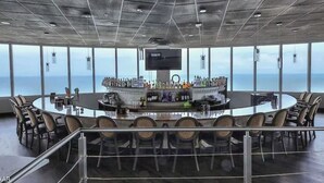 A high-ceiling conference room with a central bar, large windows, and a view of the ocean.