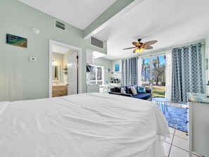 Une chambre dotée d’un grand lit, d’un ventilateur de plafond et offrant une vue sur l’extérieur grâce à une porte coulissante.