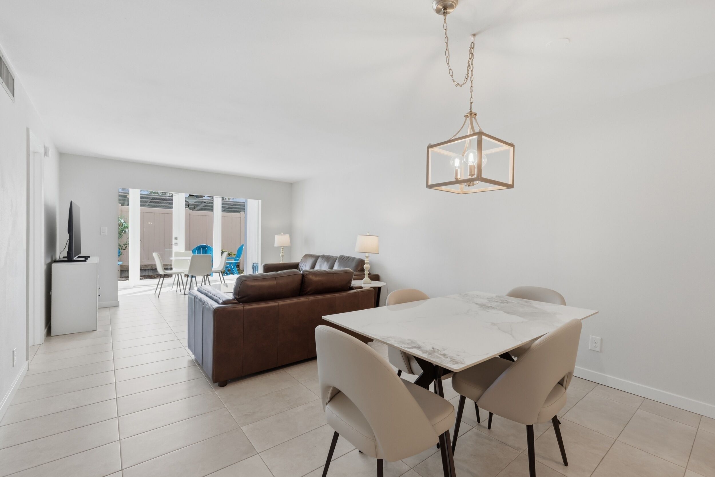 Ein modernes Wohnzimmer mit Essbereich, einem braunen Sofa, einem weißen Tisch und einer Chandelüster.
