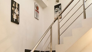 Una escala amb barana metàl·lica i graons negres, parets blanques i tres quadres emmarcades.