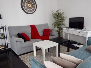A living room with a grey sofa, red and black cushions, a white coffee table, a black TV stand, and a potted plant. - RARE ! House 180m2 with terrace in historical center. (Tavira)