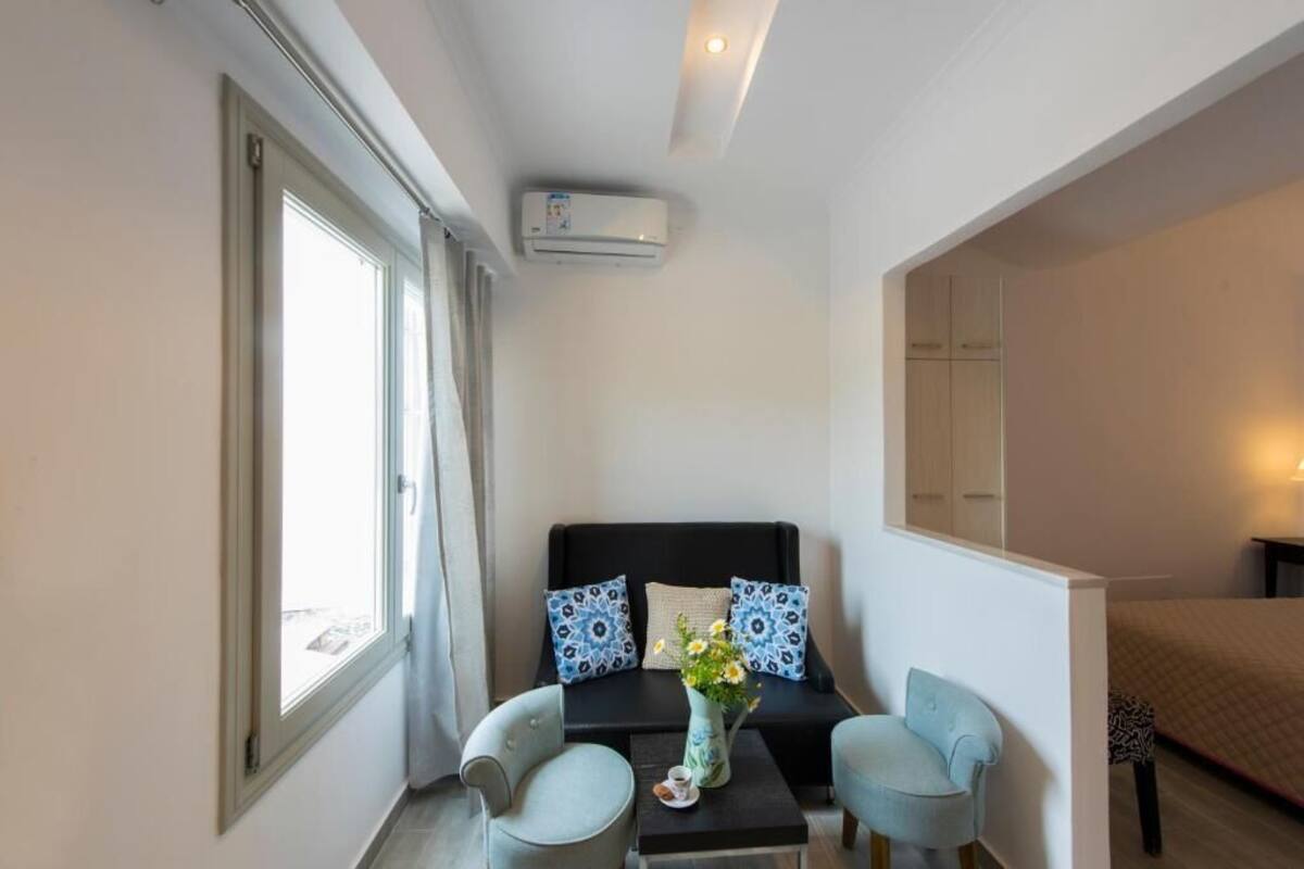 A compact hotel room with a bed, a sofa, two armchairs, a small table, and a window.