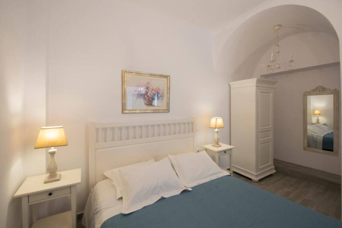 A bedroom with a bed, two bedside tables with lamps, a wardrobe, a mirror, and a framed picture on the wall.