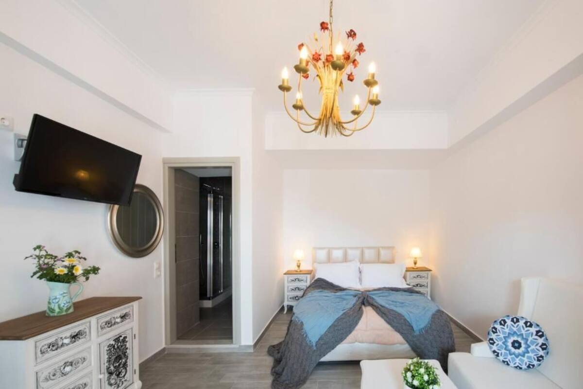 A bedroom with a bed, bedside tables, a TV, a chandelier, and a door leading to a bathroom.