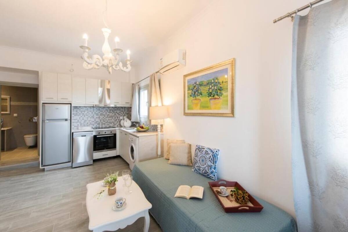 A compact kitchen with modern appliances, a dining area with a table and chairs, a sofa, and a painting on the wall.