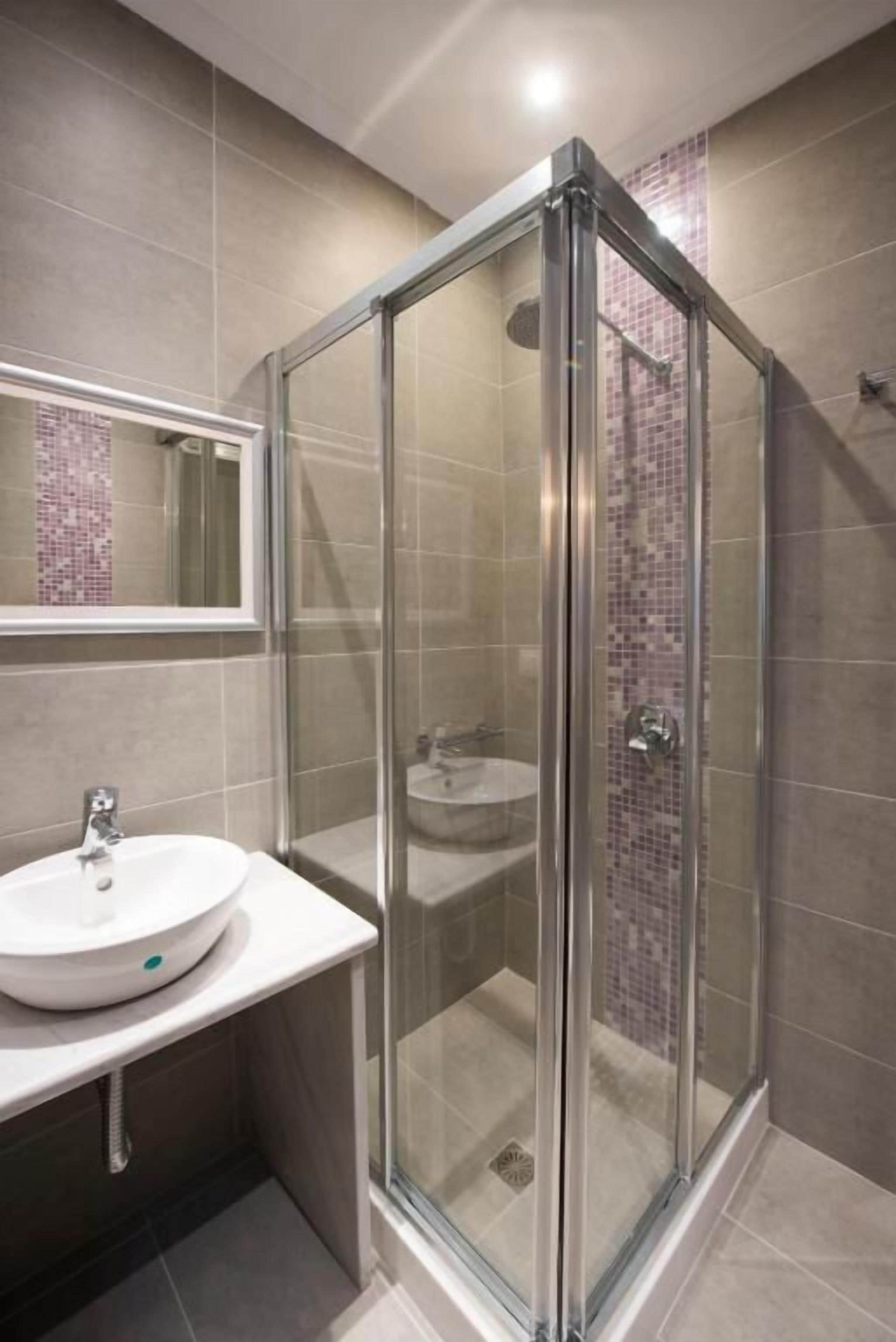 Un bany modern amb plat de dutxa envoltat de vidre, un lavabo blanc i un salvassecs revestit de rajola.