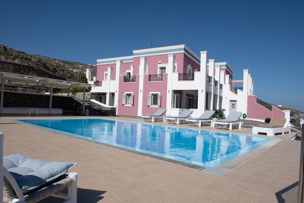 A modern hotel with a swimming pool, sun loungers, and a hillside view. - Rose Suites (Santorini)