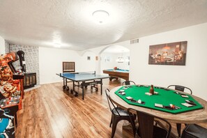 A room with a ping pong table, a pool table, and a green felt poker table.