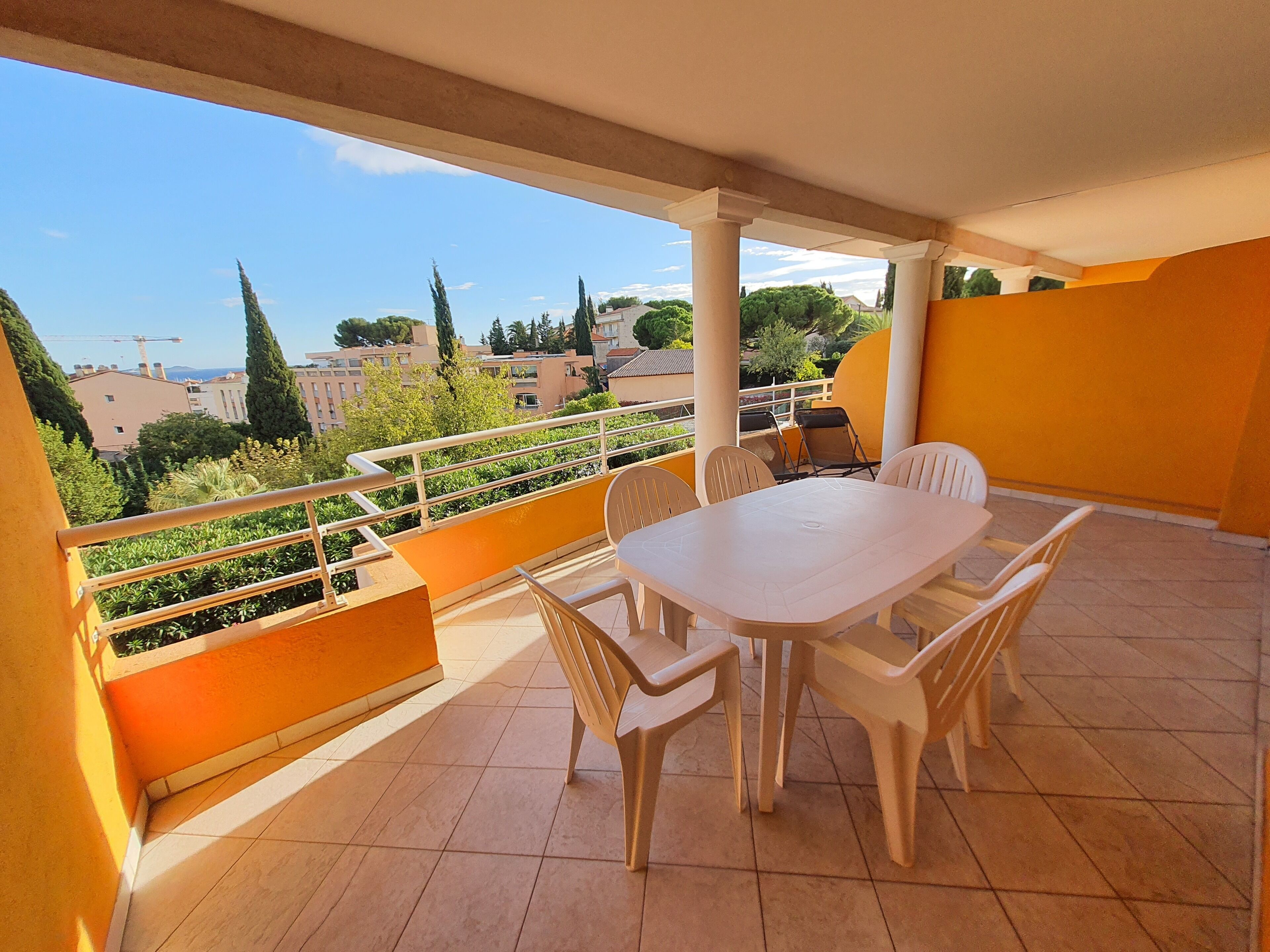A balcony with a white table and chairs, a railing, and a view of buildings and trees.