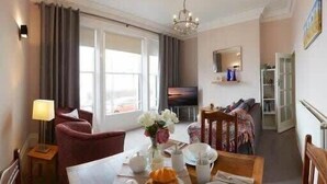 A living room with a sofa, a dining table set for two, and a television. - Crescent View - Panoramic sea views (Filey)