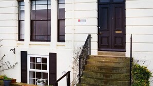 A white building with a dark brown door, a small set of stone steps, and a black metal railing. - Crescent View - Panoramic sea views (Filey)