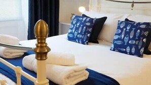 A neatly made bed with blue and white patterned pillows, a white headboard, and a blue bedspread. - Crescent View - Panoramic sea views (Filey)