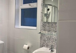 Une salle de bain avec des toilettes, un lavabo, une douche et une fenêtre avec des rideaux bleus.