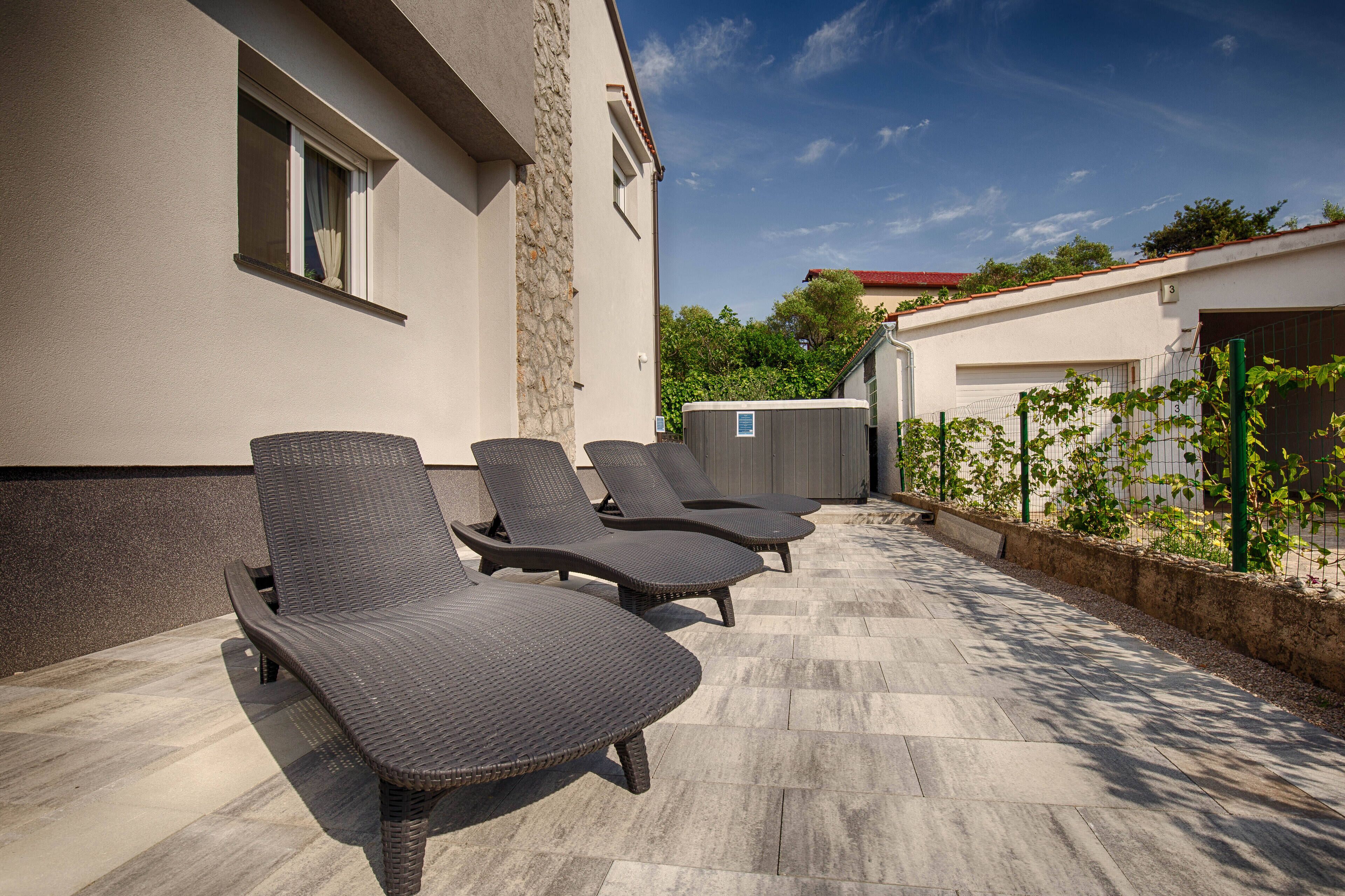Une terrasse avec trois chaises longues, un mur en pierre et un jardin clos.