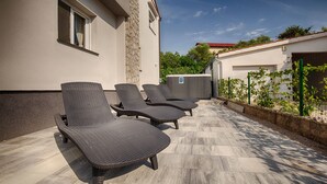 En terrasse med tre liggestole, en stenvæg og en indhegnet have.