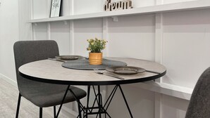 Un coin repas moderne avec une table ronde, deux chaises, une plante en pot et un tableau encadré au mur.