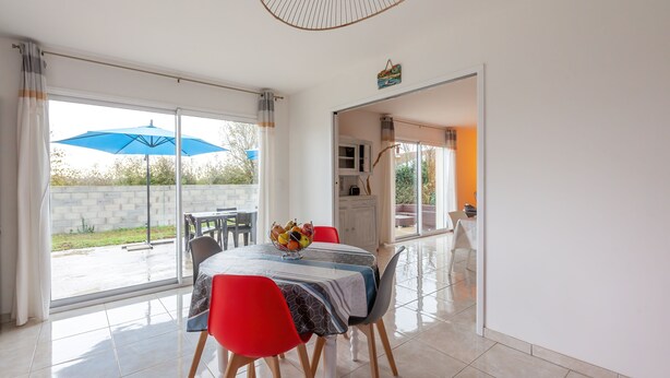 A dining area with a table set for four, a blue umbrella outside, and a view of the garden. - La Janne - Maison avec jardin (Saujon)