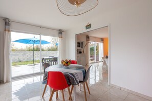 Een eetruimte met een tafel voor vier personen, een blauwe parasol buiten en uitzicht op de tuin.