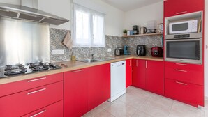 A modern kitchen with red cabinets, a stainless steel range hood, a microwave, and a dishwasher. - La Janne - Maison avec jardin (Saujon)