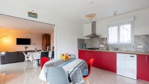 A modern kitchen with red cabinets, a white dishwasher, and a dining area with a table set for two. - La Janne - Maison avec jardin (Saujon)