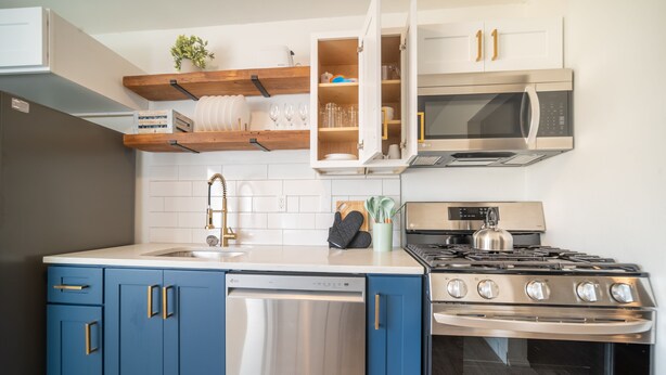 A modern kitchen with blue cabinets, a stainless steel dishwasher, a gas stove, and a microwave.