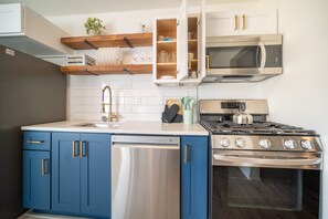 Una cocina moderna con gabinetes azules, lavavajillas de acero inoxidable, estufa a gas y microondas.