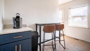 A kitchen with a coffee maker, two stools, and a trash bin.