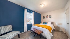 A bedroom with a bed, bench, and a window with curtains.