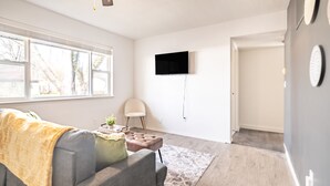 A modern living room with a gray sofa, a small table with a plant, and a television on the wall.