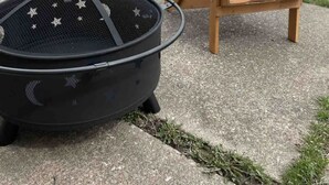 A black grill with star decorations on a concrete surface, next to a wooden Adirondack chair.