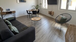 A modern living room with a dark-colored sofa, a round coffee table, a black chair, and a TV mounted on the wall. - Duplex apartment in the heart of Cassis village (Cassis)
