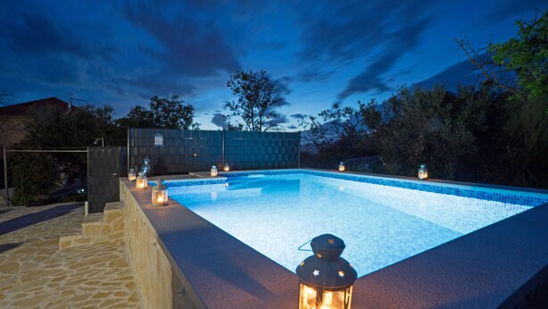 A swimming pool with a stone border and lanterns along the edge. - Casa Ambi (Trogir)
