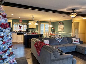 Una sala de estar acogedora con un sofá seccional gris, una pequeña zona de cocina con barra y un árbol de Navidad.