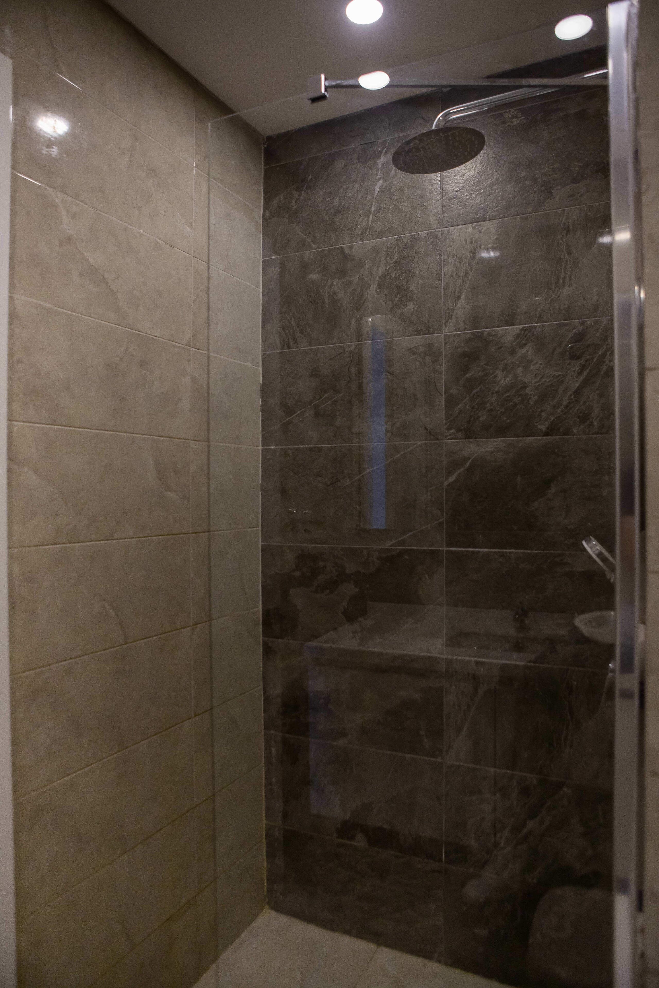 A walk-in shower with dark marble tiles and a glass door.