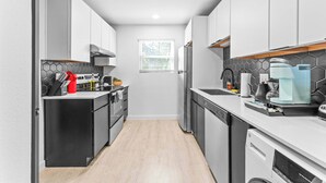 A modern kitchen with white cabinets, a black countertop, and a window with blinds. - Prime SoCo cute studio w/ laundryWiFi, 7 Min to DT (Austin)