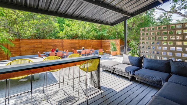An outdoor patio with a wooden deck, a covered seating area with a sofa and chairs, and a wooden fence in the background. - Prime SoCo cute studio w/ laundryWiFi, 7 Min to DT (Austin)