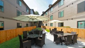 Een terras buiten met tafels en stoelen, omgeven door houten schermen en gebouwen.