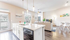A modern kitchen with a dishwasher, a dining area with a white table and chairs, a sofa, and a ceiling fan. - Comfy 2BR king suite, fast WiFi, 8 min to Downtown (Austin)