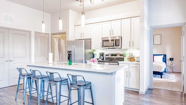 A modern kitchen with white cabinets, stainless steel appliances, and a central island with bar stools. - Comfy 2BR king suite, fast WiFi, 8 min to Downtown (Austin)
